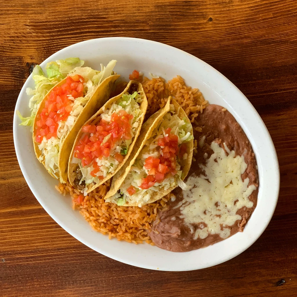 A plate of three hard-shell tacos, Spanish rice, and refried beans.