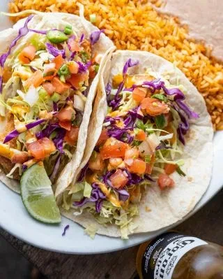 Two fried fish tacos, Mexican rice, lime, and a Corona.