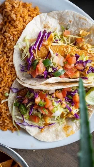 Vibrant plate of two crispy tacos with toppings and Mexican rice.