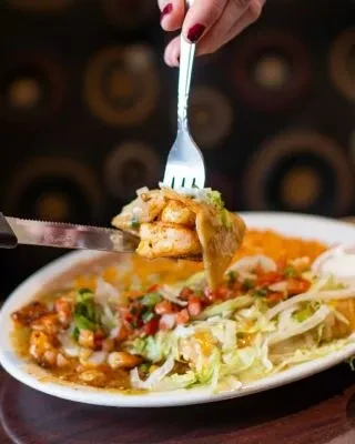 Hand with red nails forks shrimp and taco from a vibrant plate.