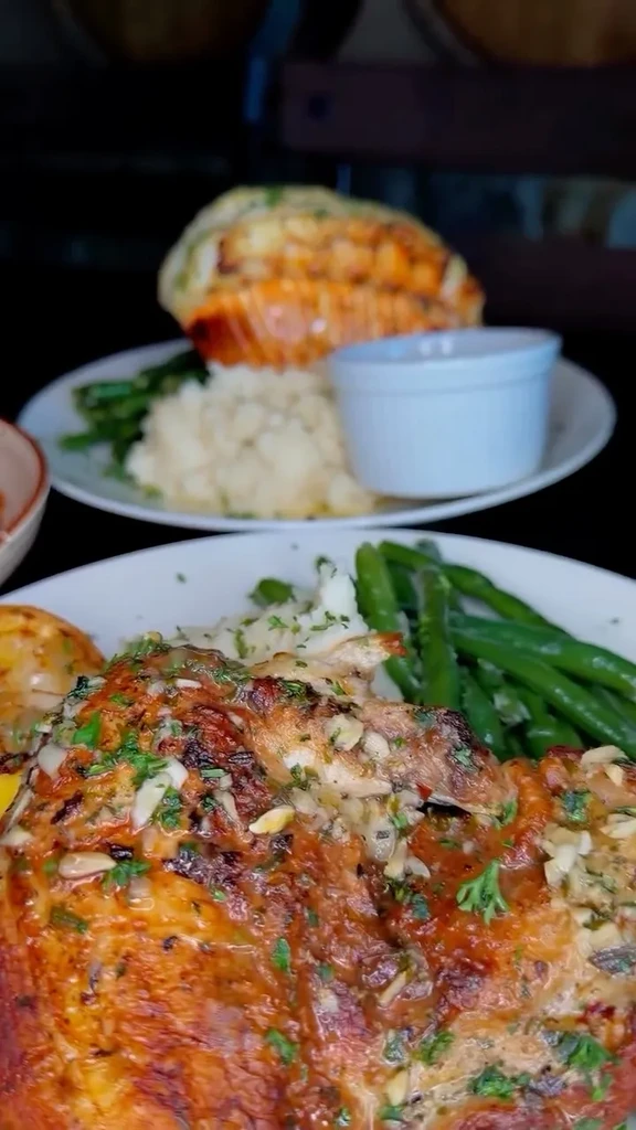 Two restaurant plates with roasted meat, vegetables, and a lobster tail.