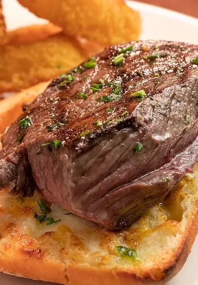 Seared medium-rare steak, green herbs, and melted cheese on toast.