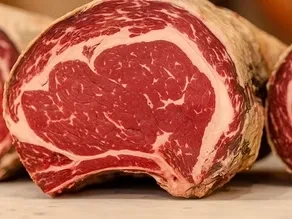Close-up of a raw, dry-aged prime cut of red meat with marbling.