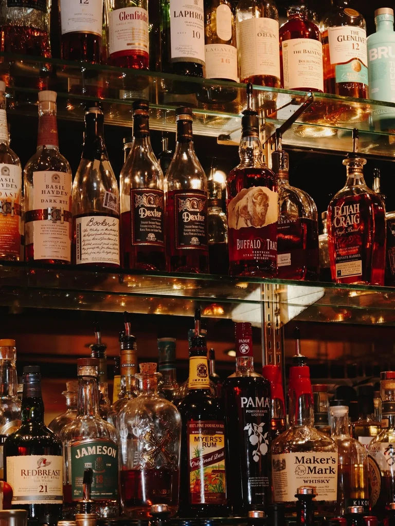 Densely packed liquor bottles on glass shelves in a dimly lit bar.