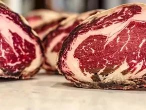 Thick, raw, highly marbled beef cuts on a light counter.
