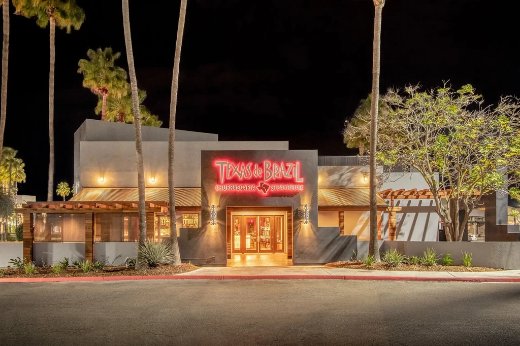 Modern Texas de Brazil Steakhouse lit at night, surrounded by palm trees.