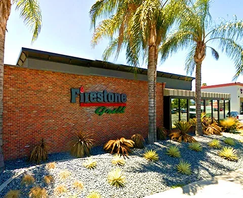 Sunny exterior of Firestone Grill, brick building, palm trees, desert landscaping.