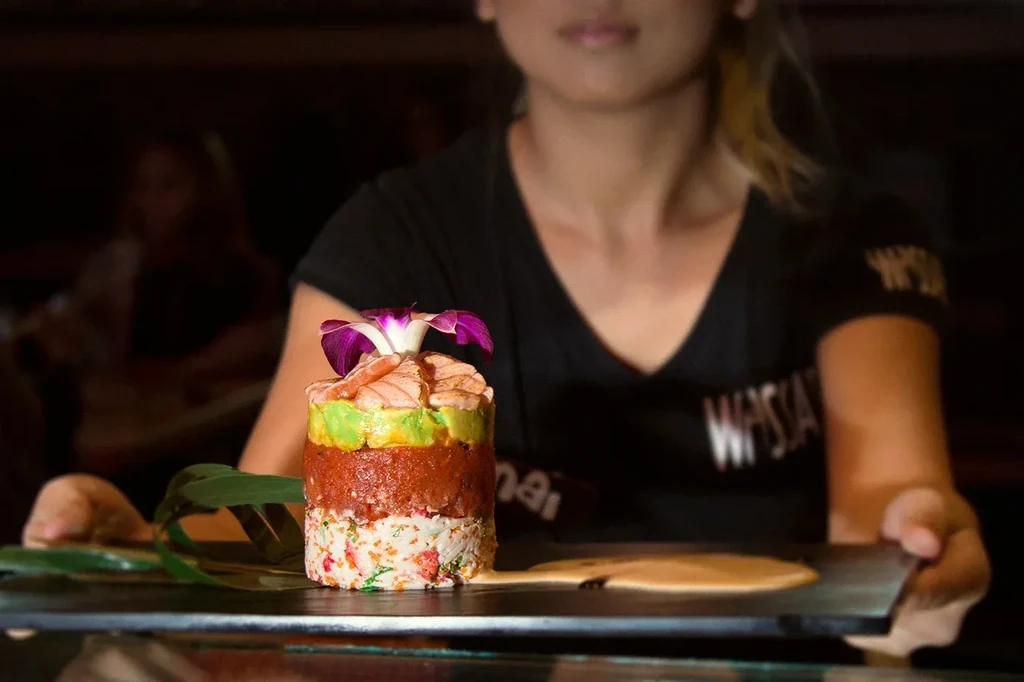 Layered sushi tower with salmon, tuna, avocado, and orchid garnish.