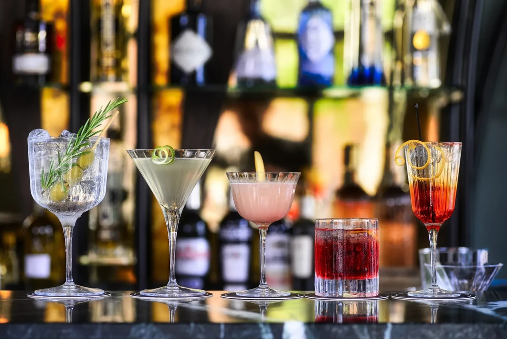 Five distinct cocktails with varied garnishes lined on a bar.