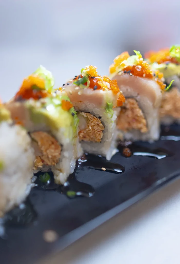Uramaki sushi with fish, avocado, tobiko, and sesame on a black plate.