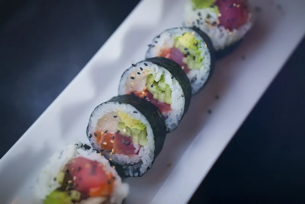 Five sushi rolls with tuna, avocado, cucumber, sesame on white plate.