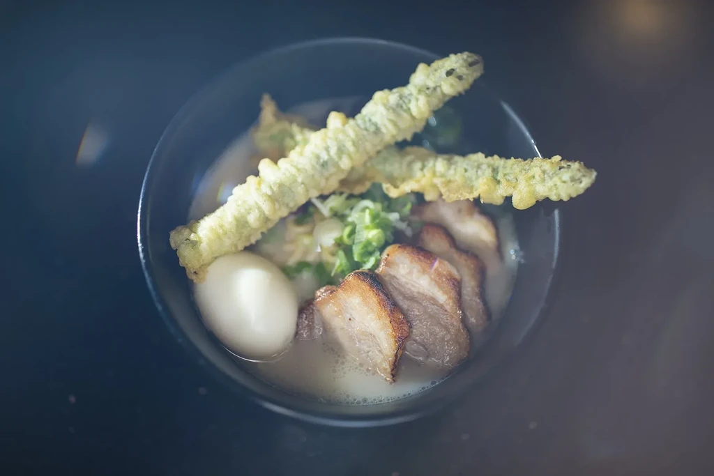 Overhead view of ramen with pork belly, egg, asparagus tempura, green onions.