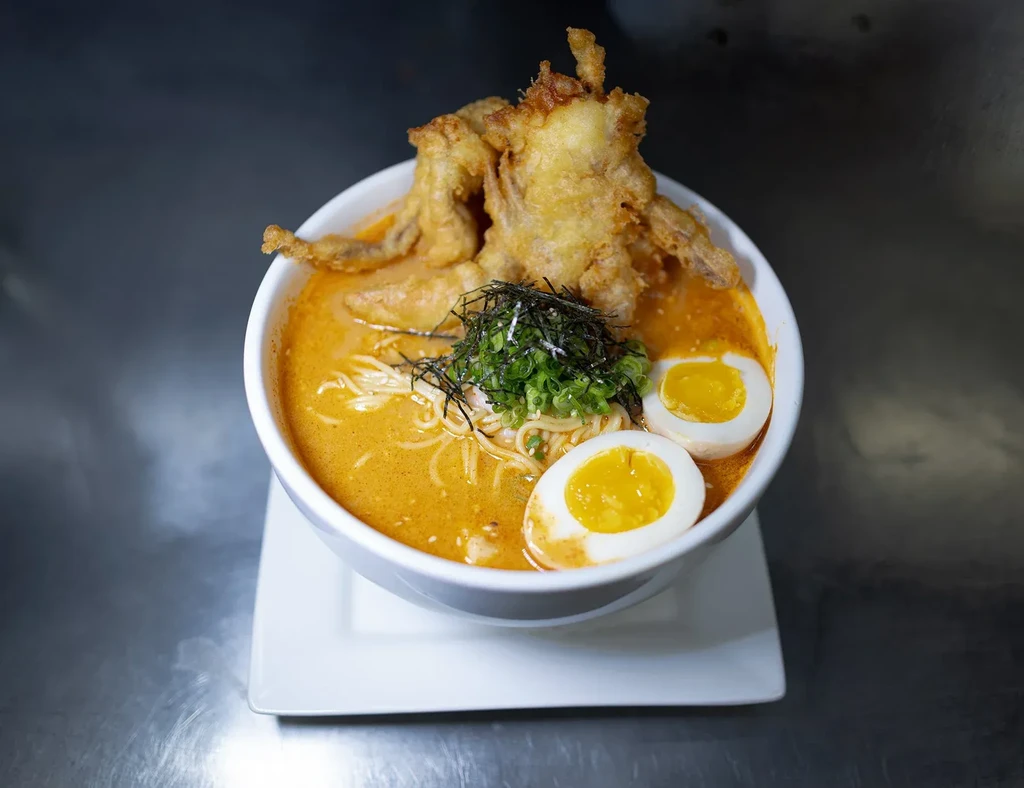 Ramen bowl with large fried item, halved eggs, and green onions.