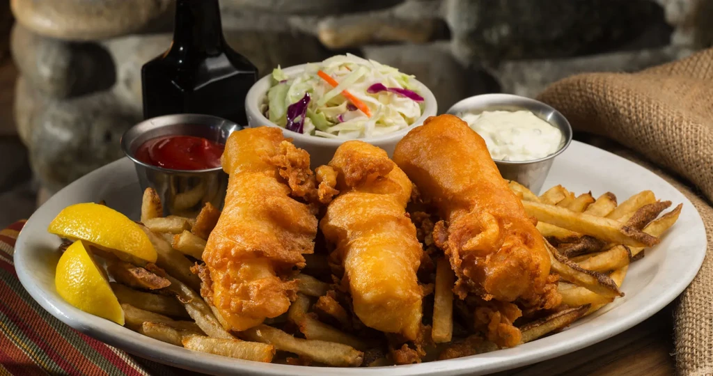 Classic fish and chips plate with lemon, sauces, and coleslaw.