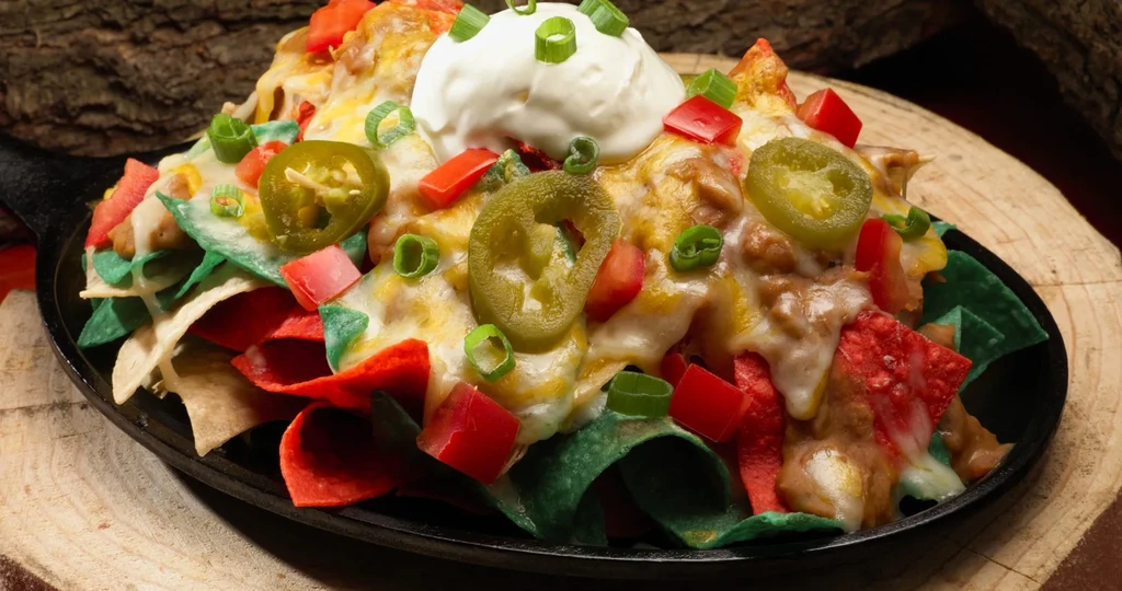 Multi-colored nachos in skillet, with cheese, meat, vegetables, sour cream.