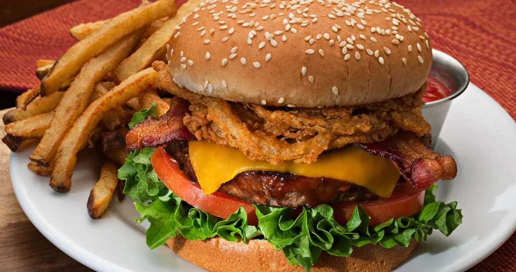Burger with melted cheese, bacon, onion rings, fries, and ketchup.