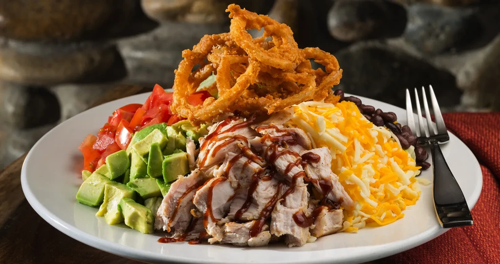 BBQ chicken, onion rings, avocado, tomatoes, cheese, black beans on a plate.