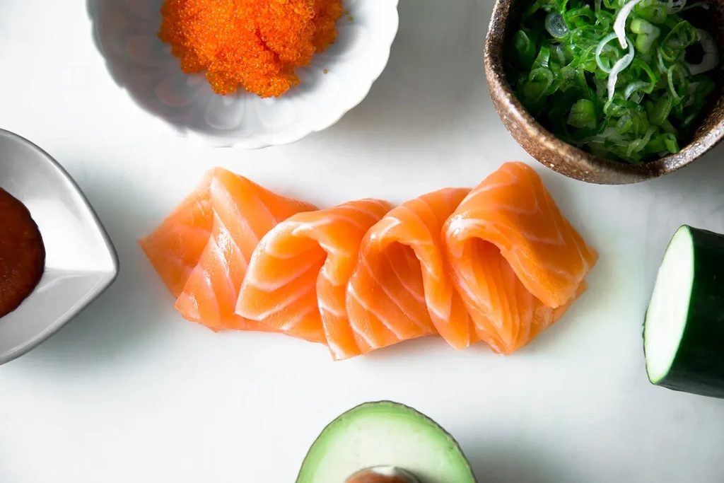 Flat lay of salmon sashimi, tobiko, avocado, and green onions.