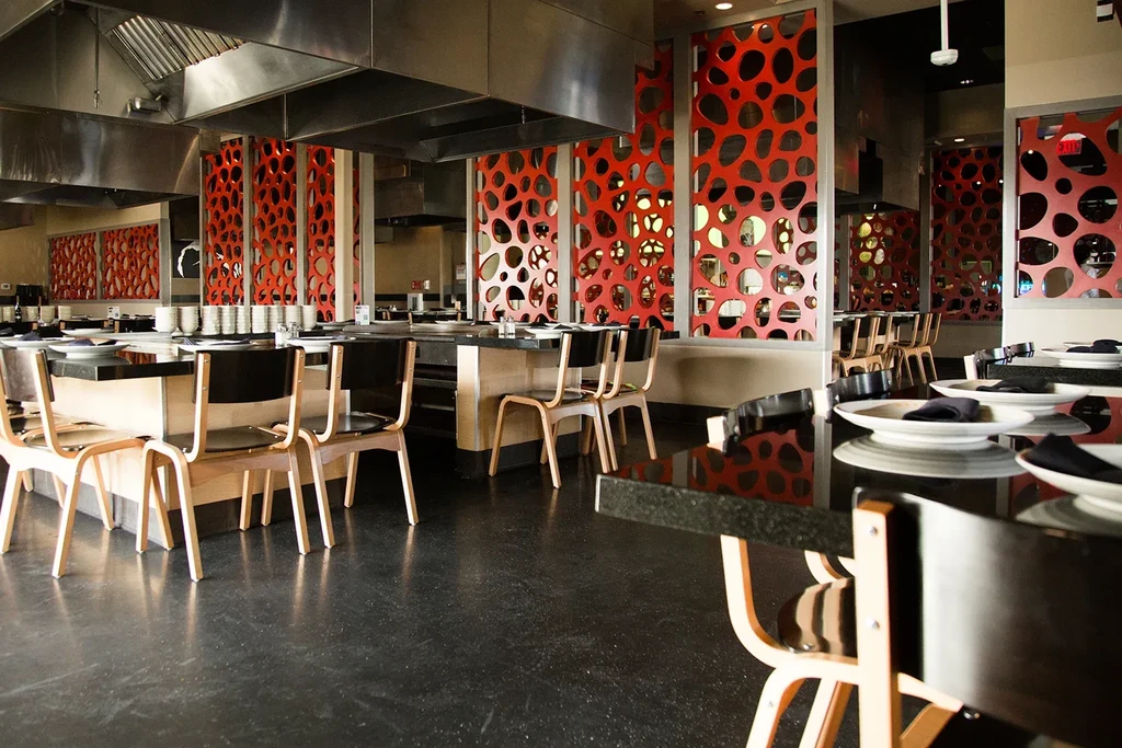 Empty modern hibachi restaurant with cooking stations and red decorative panels.