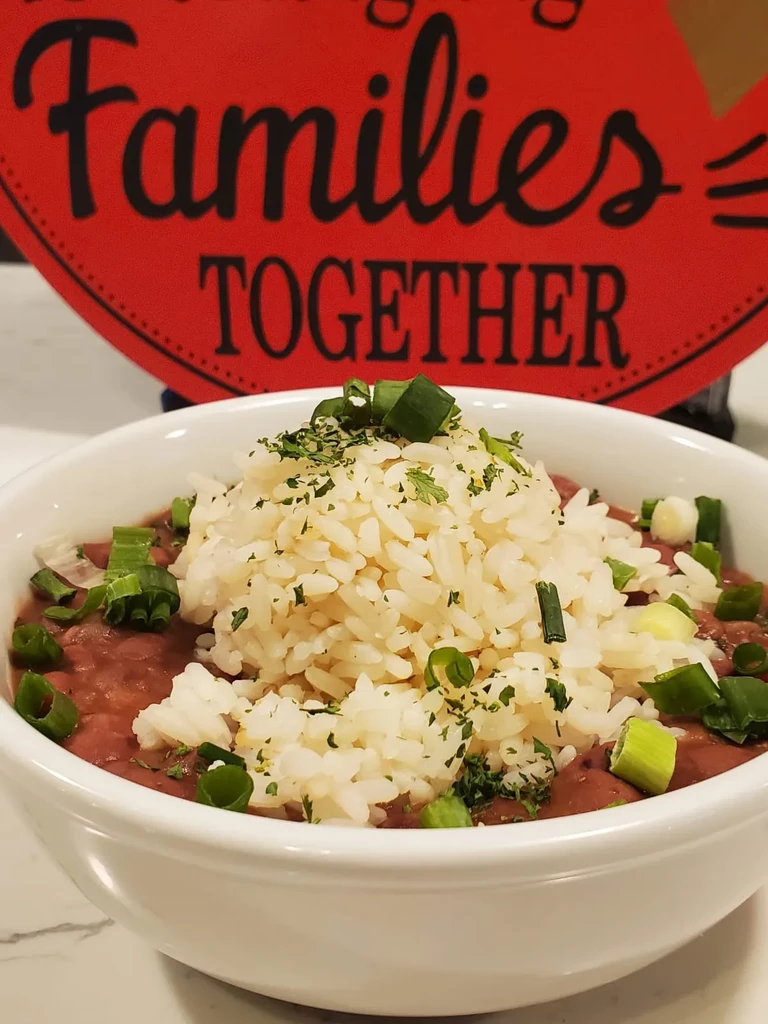 White bowl of red beans and rice topped with green onions and herbs.