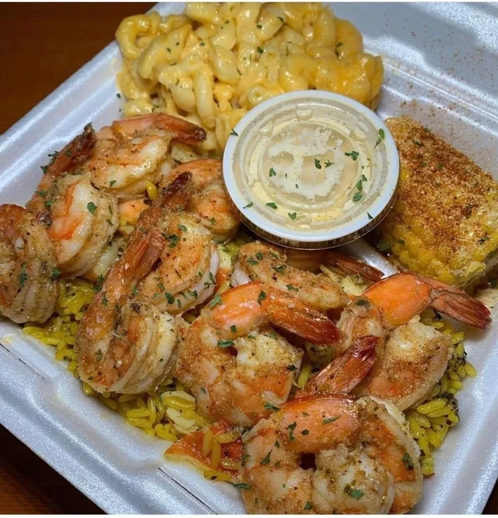 Seasoned shrimp, yellow rice, mac and cheese, corn in a takeout container.