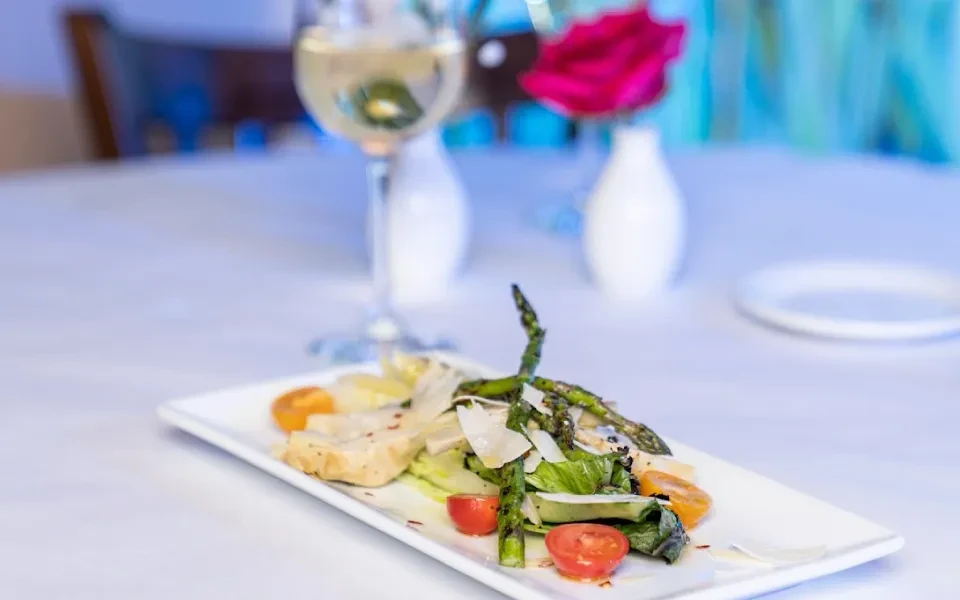 A beautifully plated meal of chicken, asparagus, tomatoes, parmesan, and wine.