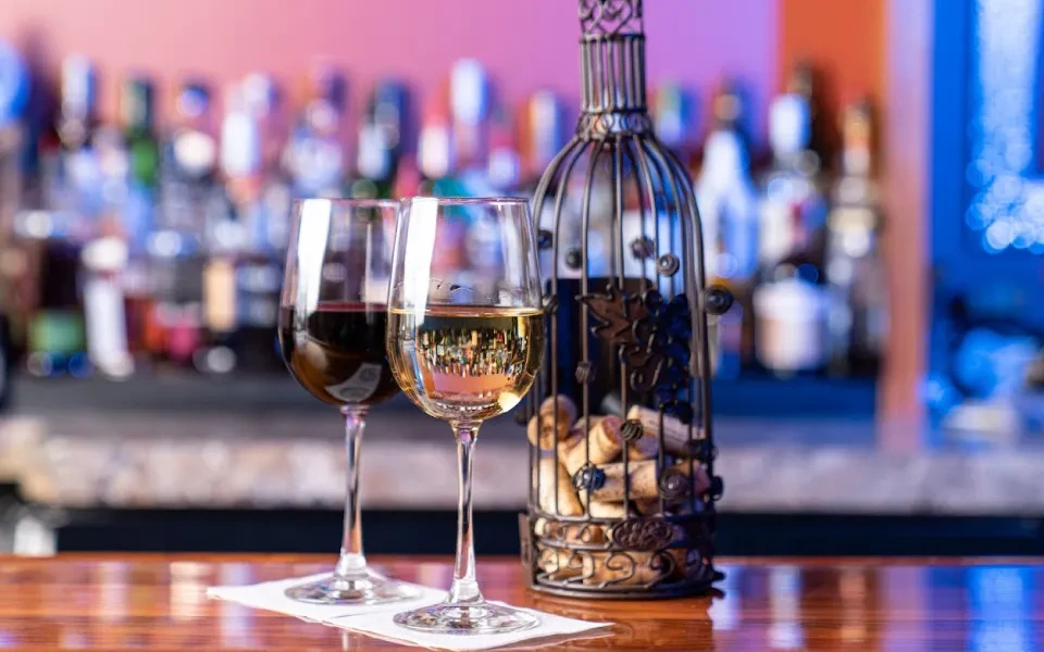 Red and white wine glasses, cork holder, on a wooden bar.