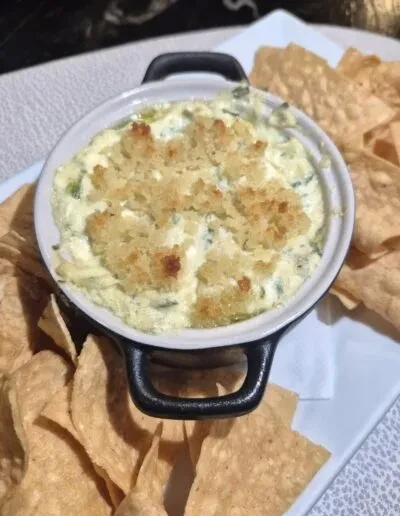 Warm, creamy dip with golden topping and tortilla chips on a white plate.