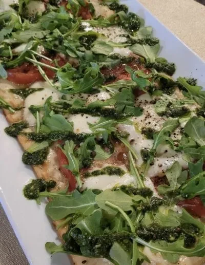Rectangular flatbread pizza with mozzarella, tomatoes, arugula, pesto, and pepper.