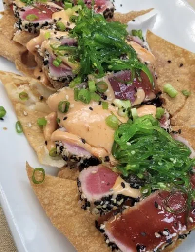 Dish of seared sesame tuna, wonton chips, creamy sauce, and wakame.