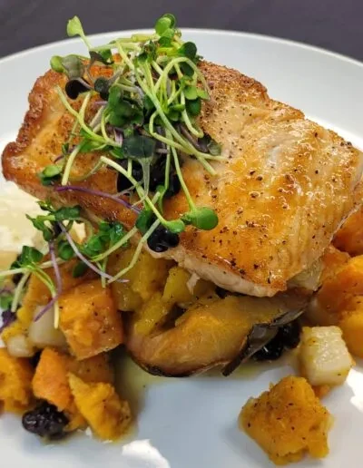 Pan-seared fish, microgreens, and roasted vegetables on a white plate.