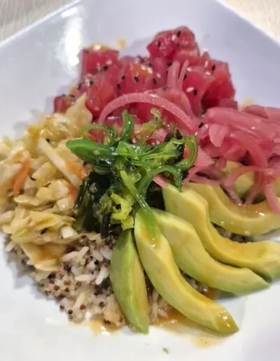 Colorful poke bowl with tuna, avocado, seaweed salad, and pickled onions.