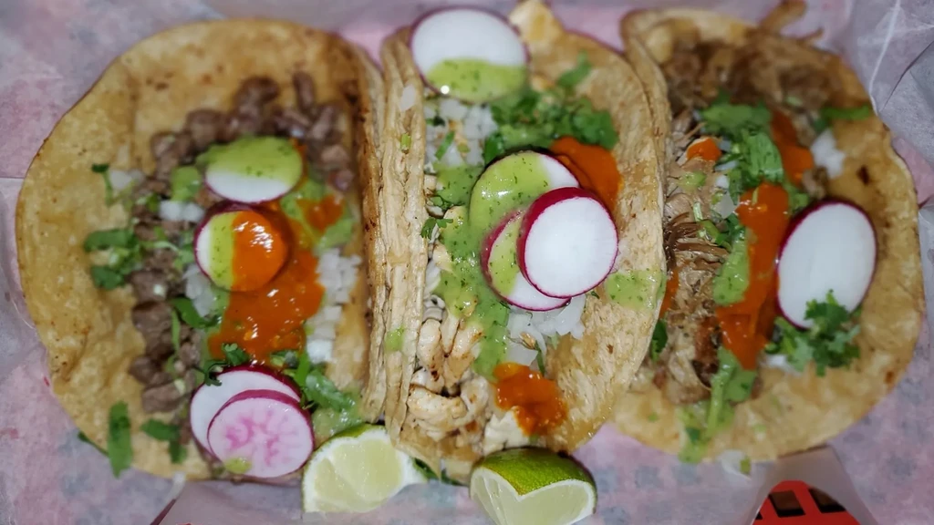 Three soft corn tacos with assorted meats, cilantro, onions, sauces, radishes.
