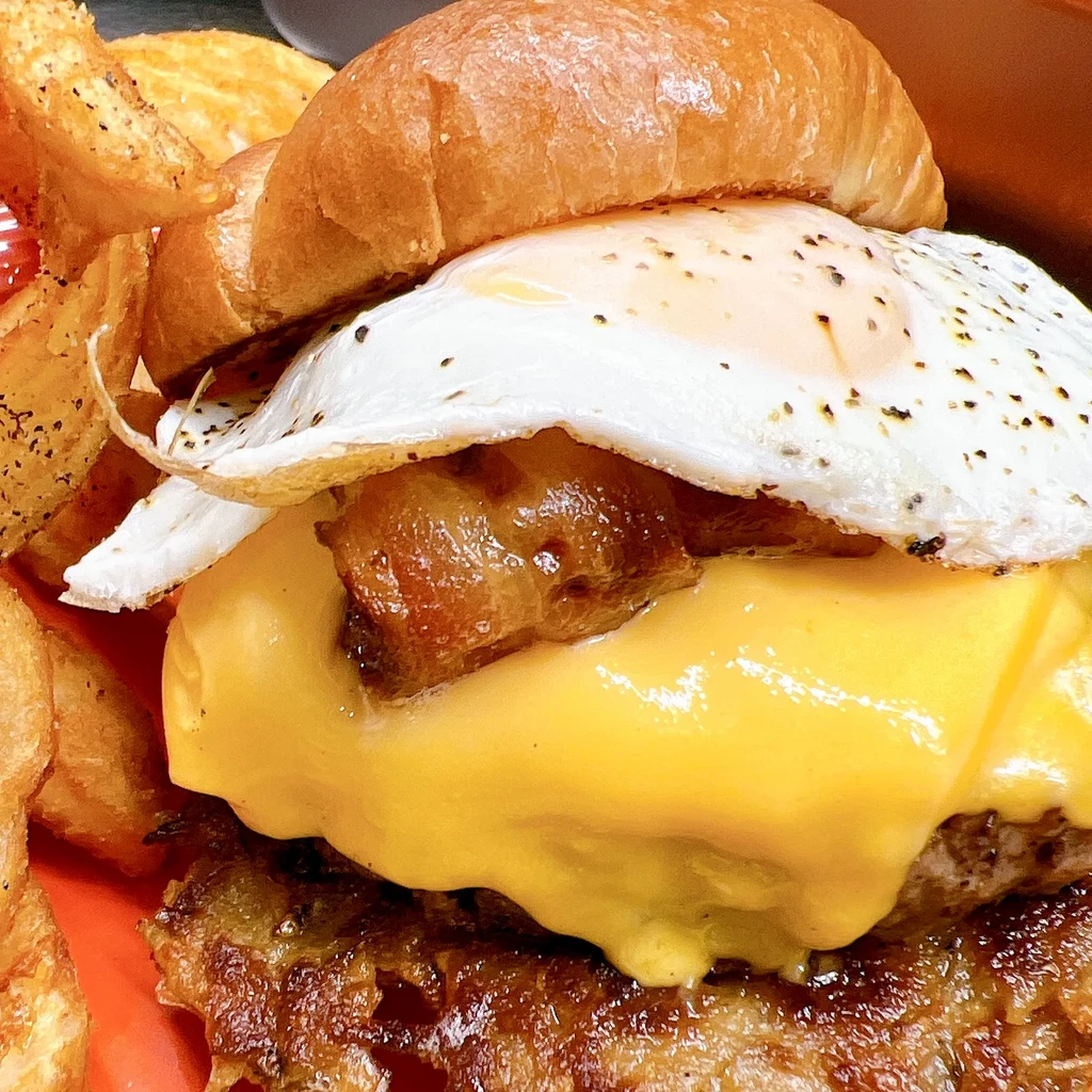 Loaded burger with fried egg, cheese, bacon, and wedge fries.