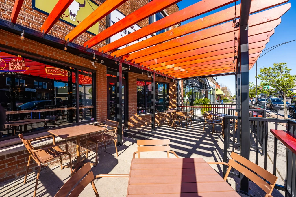 Restaurant patio with orange-slatted pergola, tables, and striped shadows.