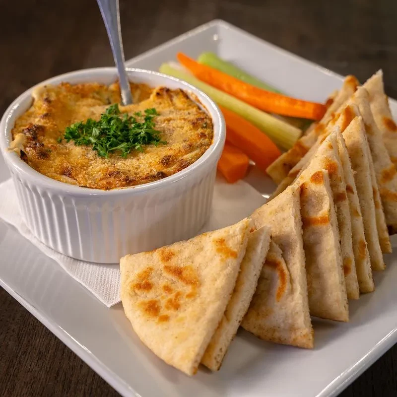 Golden-brown baked dip, pita, and vegetable sticks on a white plate.