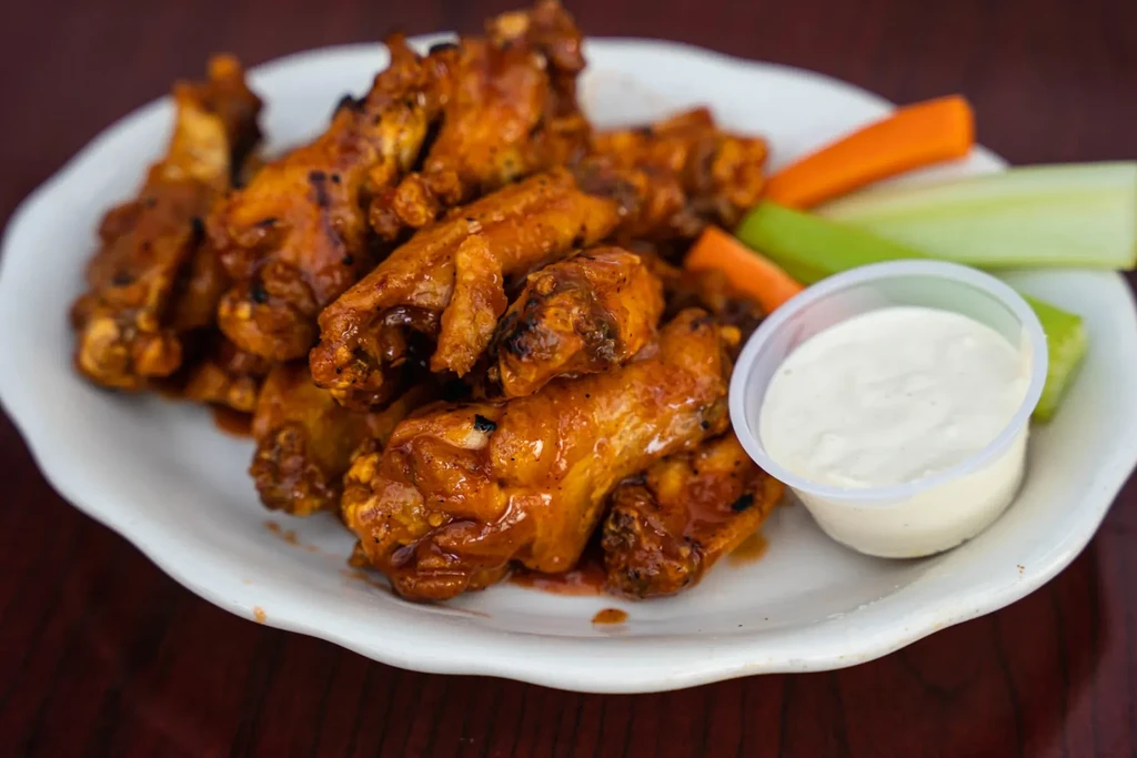 Close-up of saucy chicken wings with carrots, celery, and dipping sauce.