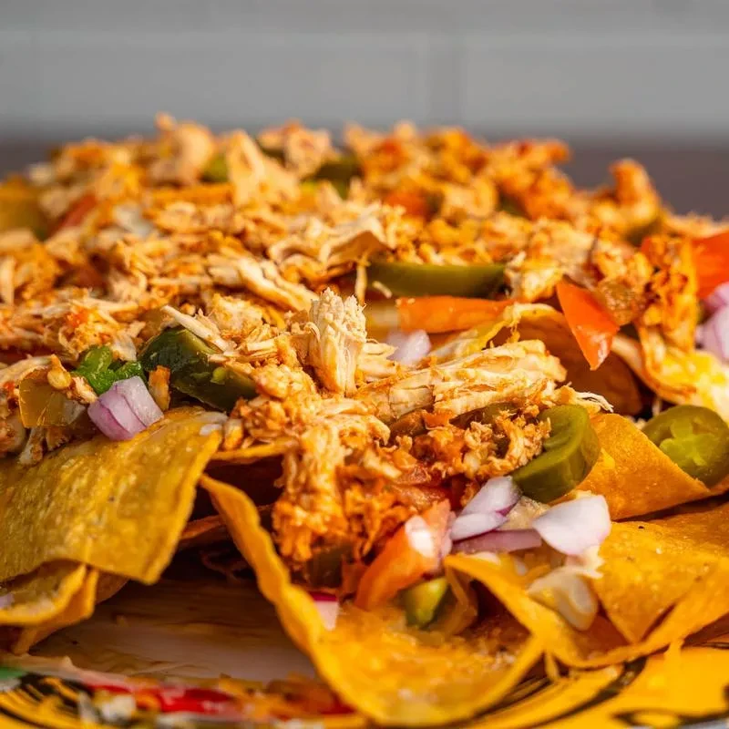 Plate of loaded nachos with chicken, cheese, jalapeños, and red onions.
