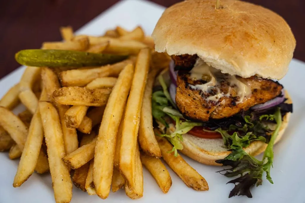 Grilled chicken burger with creamy sauce, golden fries, and a dill pickle.