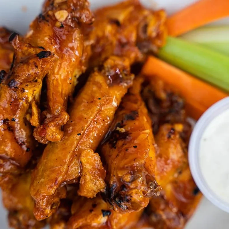 Charred orange-red glazed chicken wings, carrots, celery, and dip.