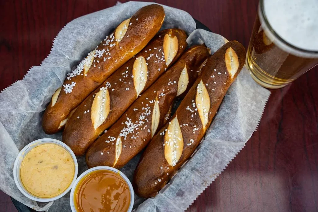Salted pretzel sticks, mustard sauce, a dark sauce, and frothy beer.