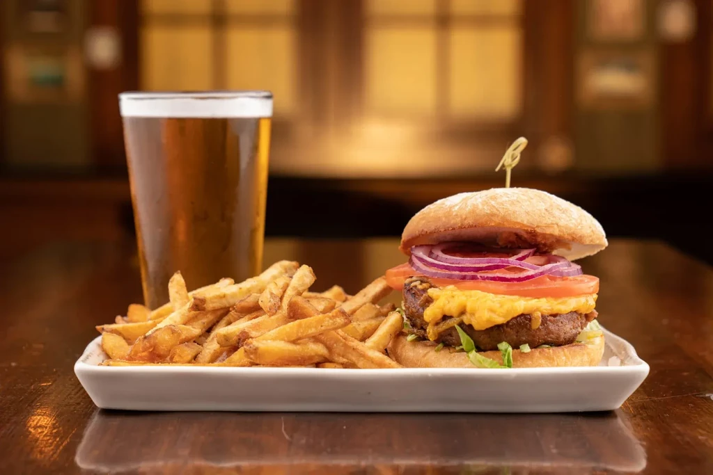 Close-up of a gourmet burger, fries, and beer in a restaurant.