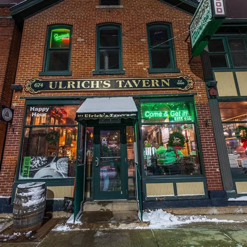Snowy Ulrich's Tavern exterior, brick building with illuminated neon signs at dusk.