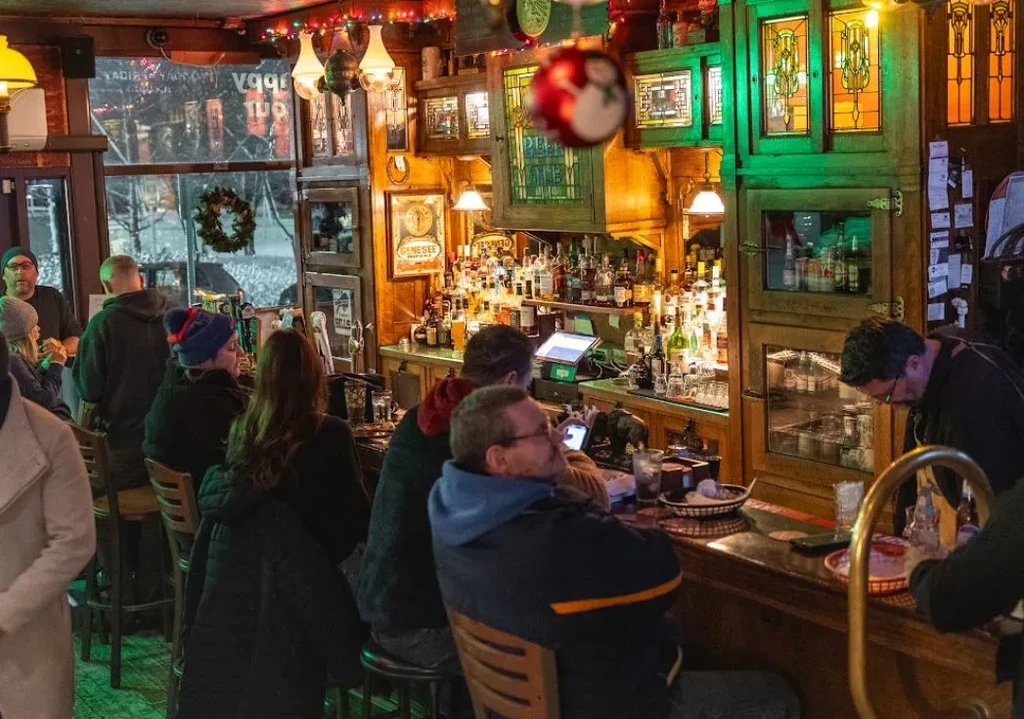 Warm traditional pub interior with a well-stocked bar, wooden decor, and patrons.