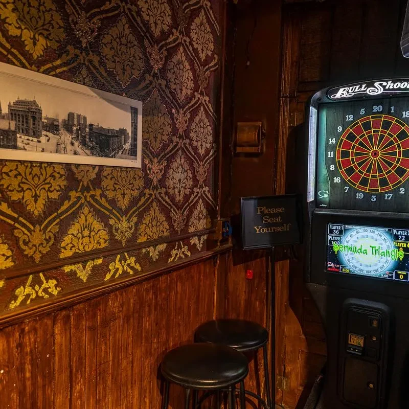 Vintage bar corner with active dartboard, bar stools, ornate wallpaper.