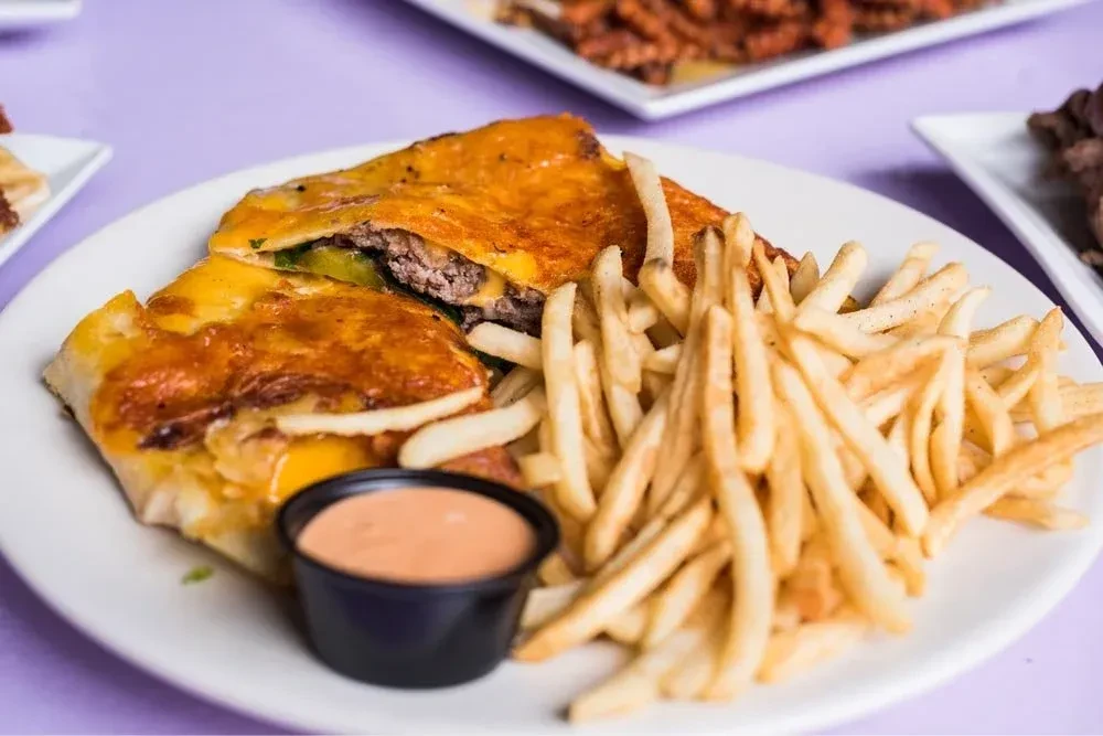 Quesadilla burger cut in half, with fries and pink dipping sauce.