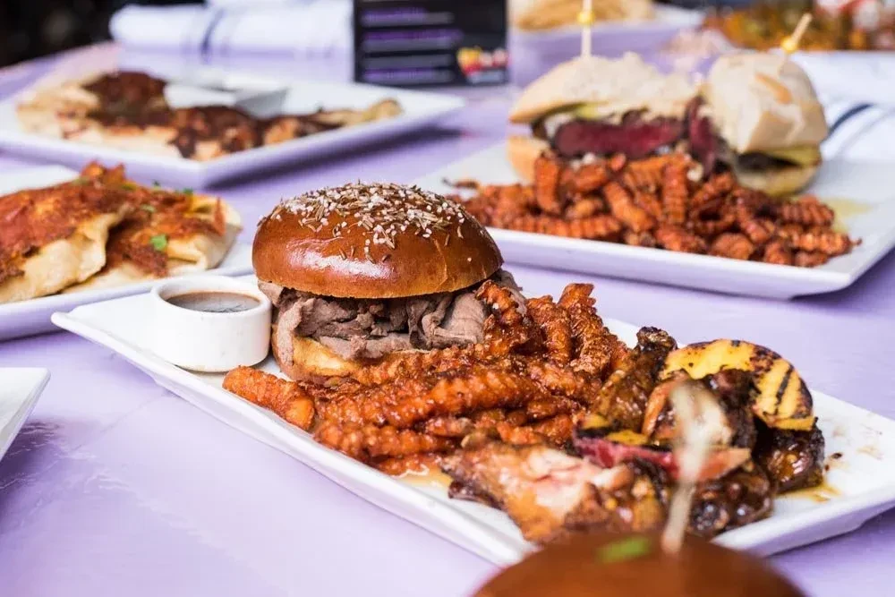 Table spread of sandwiches, waffle fries, grilled pineapple, and pizza.