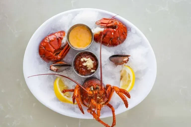 Cooked red lobster platter with sauces and lemon on crushed ice.