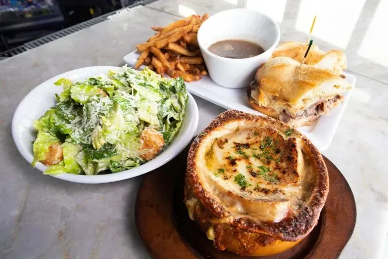 Spread of Caesar salad, French dip, fries, and French onion soup.