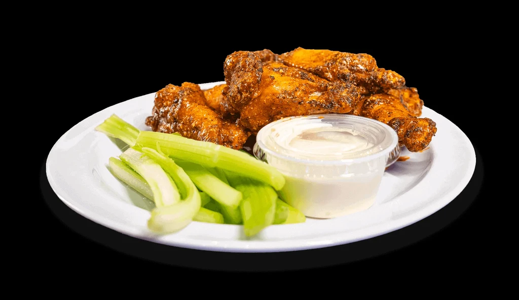 Piled chicken wings, celery sticks, and dip on a white plate.